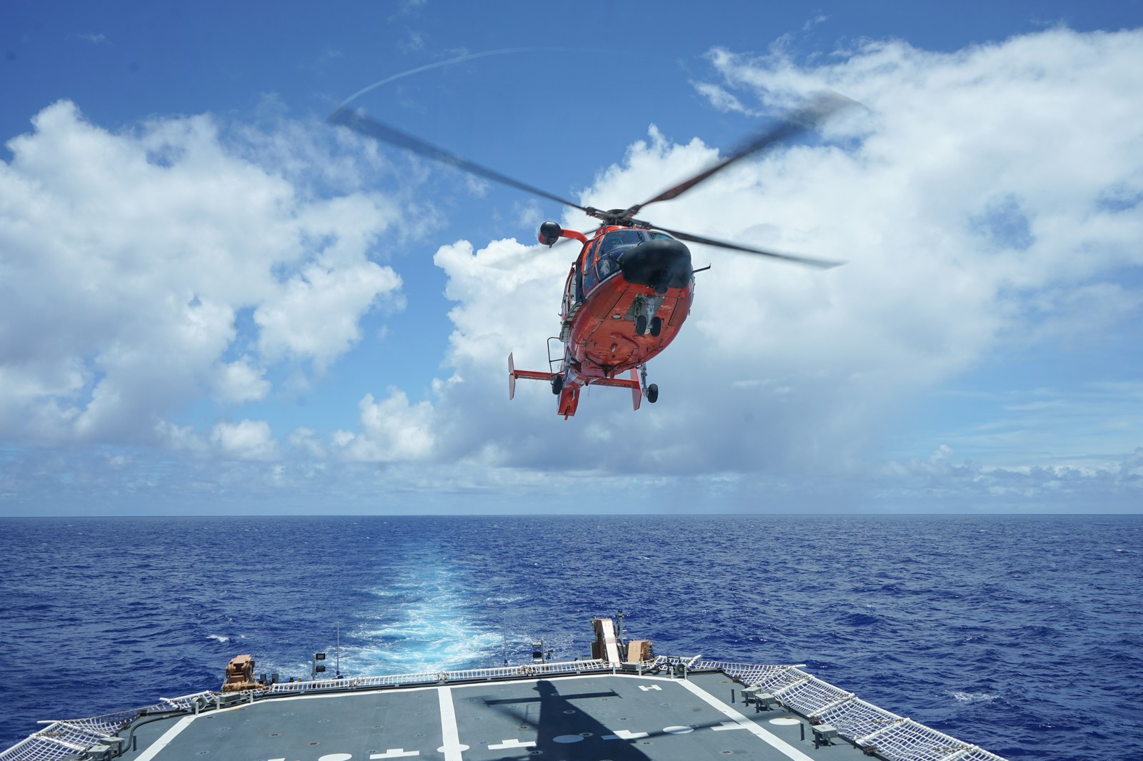 A U.S. Coast Guard helicopter conducting maritime flight operations over a cutter flight deck