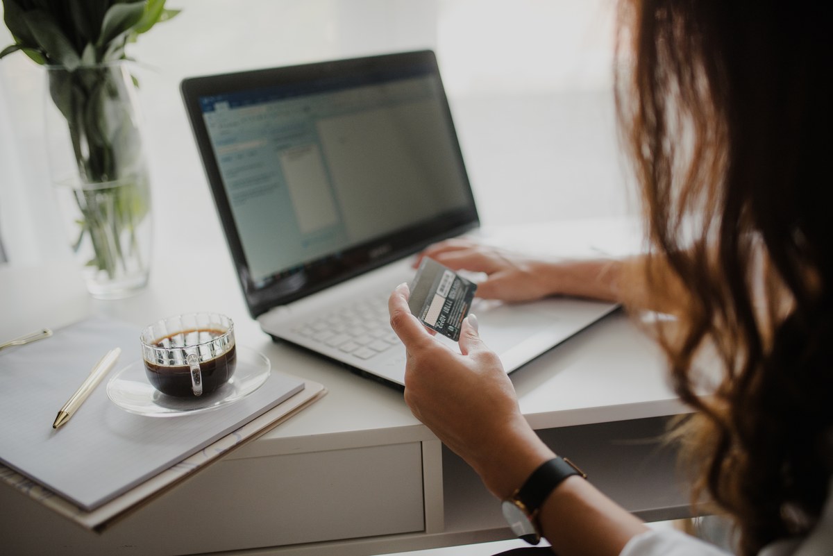 A woman seated at a desk holding a credit card while reviewing recurring billing charges on her laptop