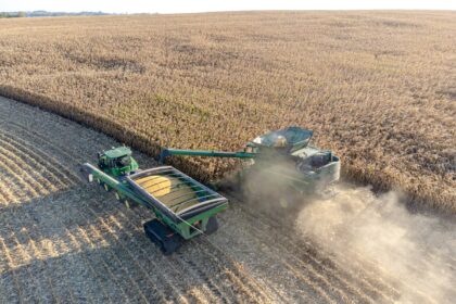 A large commercial combine harvester and tractor unloading grain in a Midwestern field