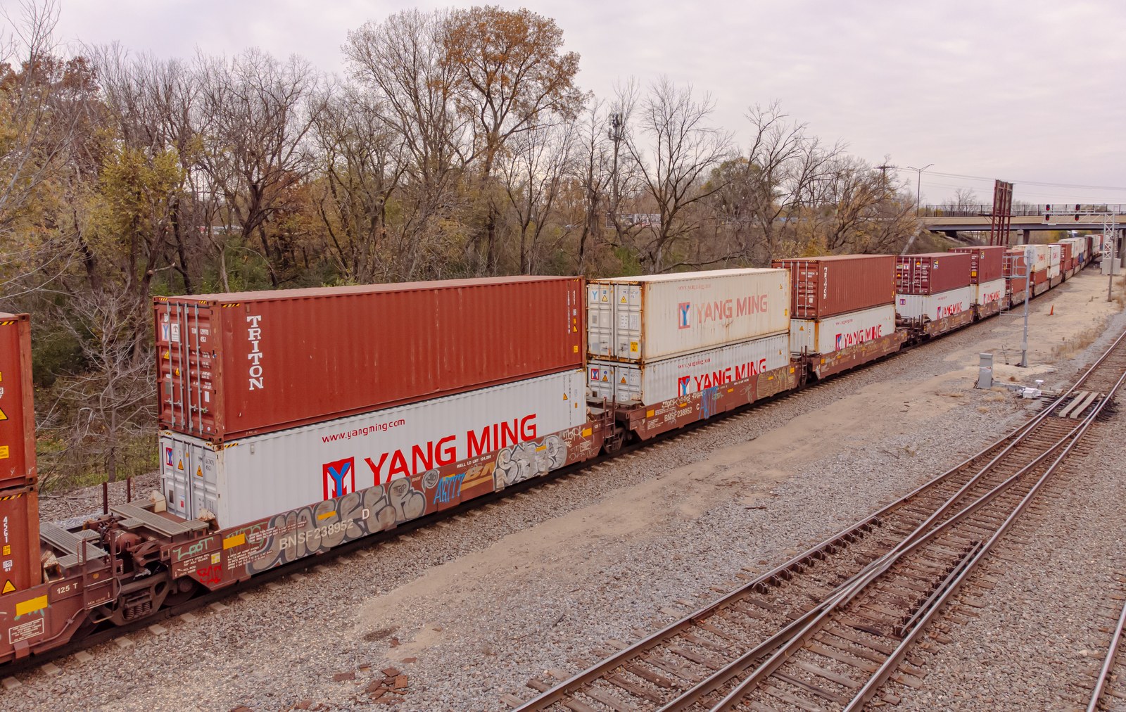 Double-stacked domestic and international shipping containers moving along a heavy freight railroad line