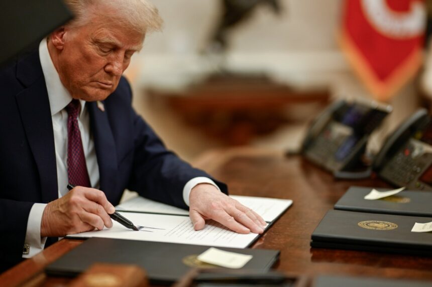 President Donald Trump seated at the Resolute Desk signing executive orders